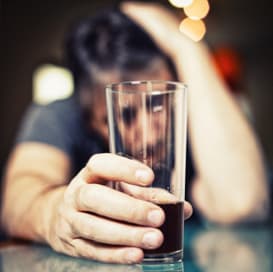 Мужчина за столом смотрит на стакан с алкоголем