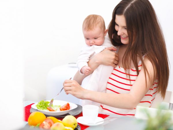 Женщина с ребёнком на руках ест салат